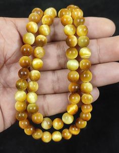 a hand holding two strands of yellow tiger's eye beads