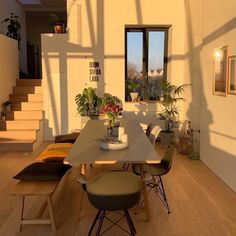 a dining room table with chairs and potted plants on top of it in front of stairs