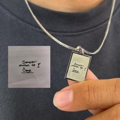 a person holding a small square pendant with writing on it