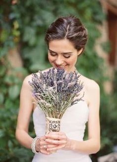 a woman in a white dress holding a bunch of lavenders and looking at the camera