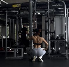 a woman squatting down in front of a gym machine