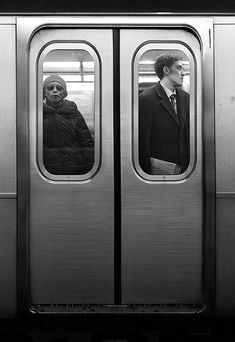 two people are standing in the door of a subway car, one is wearing a suit