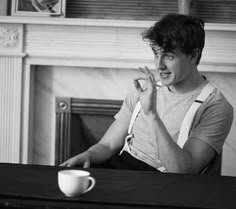 a man sitting at a table with a coffee cup in front of him and his hand up to his mouth