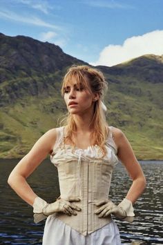 a woman standing in front of a body of water with her hands on her hips