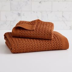 two brown towels folded on top of each other in front of a white tile wall