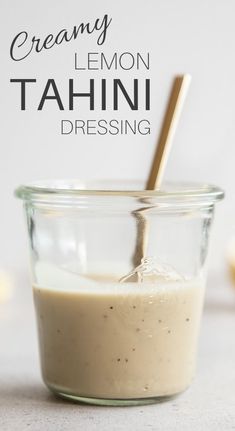 a glass jar filled with creamy lemon tahini dressing and a wooden spoon in it