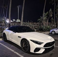 a white sports car parked in a parking lot next to some palm trees at night