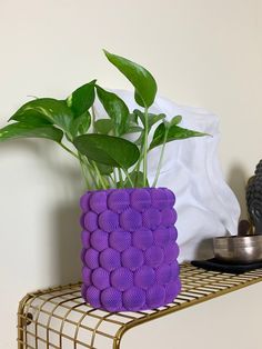 a purple vase sitting on top of a metal shelf next to a potted plant