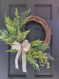 a wreath with a bow hanging on the front door is decorated with green leaves and branches