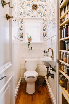 a white toilet sitting inside of a bathroom next to a sink and wooden flooring