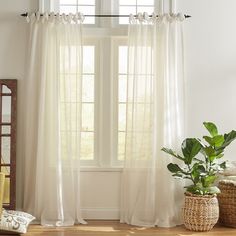 a living room with a large window and white curtains on the windowsill, along with a potted plant