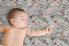 a baby laying on top of a bed next to some fish wallpaper in the background