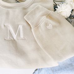 a white sweatshirt with the letter m on it next to some flowers and other items