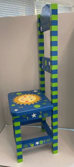 a blue and green wooden chair with a lion painted on the seat, sitting in front of a white wall