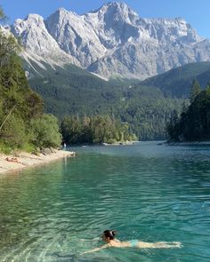 a person swimming in a lake with mountains in the background and trees on both sides