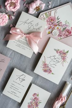 the wedding stationery is laid out with pink flowers and ribbons on it's cards