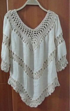 a white blouse with crochet on it hanging from a hanger in front of a wooden door