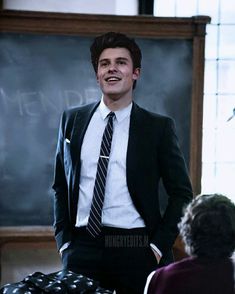 a man wearing a suit and tie standing in front of a chalkboard