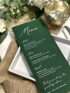 a green menu sitting on top of a white plate next to a vase with flowers