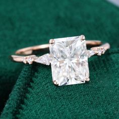 a cushion cut diamond engagement ring with two side stones on it's band, sitting on a green velvet surface