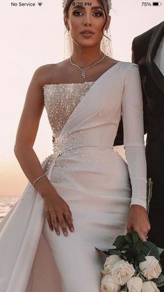 a bride and groom posing for a wedding photo in front of the ocean at sunset