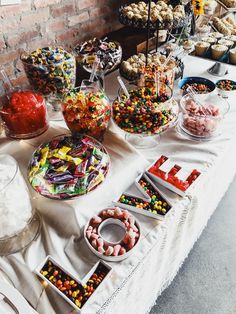 a table topped with lots of different types of candies and desserts next to a brick wall