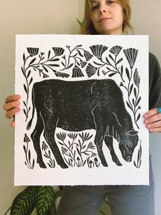 a woman holding up a black and white print with an image of a cow in the middle