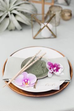 a plate with chopsticks and flowers on it sitting on a white table cloth