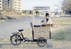 a woman sitting at a food cart with a bike parked next to her on the side