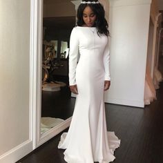 a woman standing in front of a mirror wearing a white dress with long sleeves and a high neckline