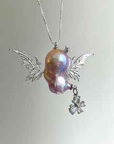 Elevate your elegance with this exquisite necklace that features a unique pendant designed to resemble an angel, featuring a lustrous baroque pearl. This stunning blend of natural beauty and exquisite craftsmanship floats with two large silver wings, with a dangling crystal butterfly and a twinkling star, providing a harmonious balance to the overall design. Whether you seek a distinctive touch for your evening attire or a fresh accent for your everyday jewelry, this piece is a perfect addition Silver Baroque Necklace With Pearl Charm, Silver Baroque Necklace With Pearl Pendant, Luxury Baroque Pearl Silver Necklace, Fairy Pearl Necklace, Luxury Baroque Pearl Pendant Jewelry, Angel Jewelry, Silver Wings, Sustainable Jewelry, Pearl Charms