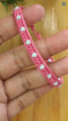 a hand holding a pink and white crochet bracelet on it's fingers