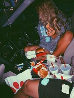 two people sitting in the back seat of a car eating fast food and drinking soda