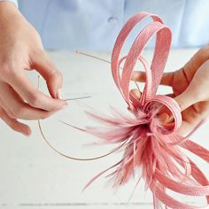 two hands are working on some type of decoration with pink ribbon and thread, while another hand is holding the string