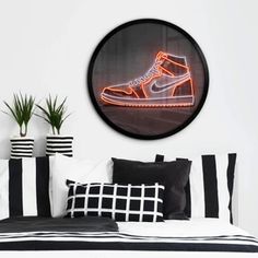 a bed with black and white pillows and a neon shoe on the wall above it