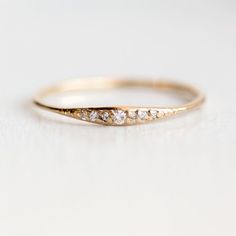 a gold wedding ring with five diamonds on it's side, sitting on a white surface