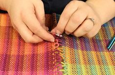 a woman is working on a colorful piece of fabric with her hands and needle in the middle