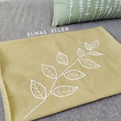 two pillows with embroidered leaves on them sitting on a couch next to one pillow and the other