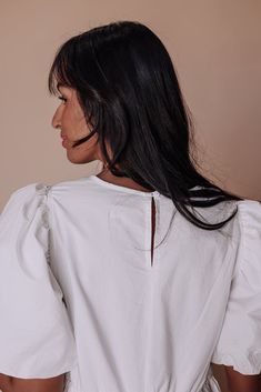 a woman with long black hair wearing a white shirt and jeans, looking off to the side