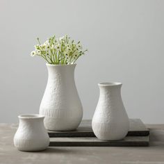 three white vases sitting on top of a wooden table next to each other with flowers in them