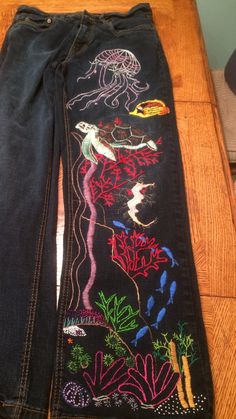 a pair of jeans with an embroidered design on the bottom and side, sitting on a wooden table