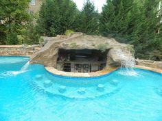 an outdoor swimming pool with waterfall and rock wall, surrounded by green trees in the background