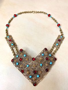 "Stunning vintage Edwardian era gilt brass filigree necklace. This gorgeous necklace was designed around a former antique sash belt. It was carefully deconstructed and refashioned into a dramatic necklace.  The large curved, dimensional filigree focal pendant is set with blue and red bezel set stones. It measures a grand 4-1/2\" x 3-1/2\". I added the original rectangular panels and linked them with textured brass chain.  I added vintage Cherry Tree brand beads to match the existing beads in the Vintage Red Ceremonial Necklace, Vintage Blue Ceremonial Jewelry, Red Filigree Vintage Jewelry, Vintage Bronze Necklace With Intricate Design, Vintage Ceremonial Necklace With Antique Finish, Vintage Gold Necklaces With Patina, Vintage Antique Finish Necklace For Ceremonial Occasion, Ceremonial Vintage Necklace With Antique Finish, Red Bohemian Filigree Jewelry