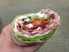 a hand holding a sandwich with meat, cheese and lettuce in it's wrapper