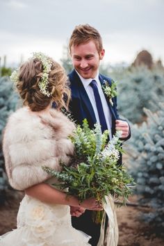 a man in a suit and tie holding a bouquet of flowers next to a woman wearing a fur coat