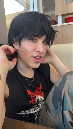 a young man with black hair and piercings on his ears sitting in a chair