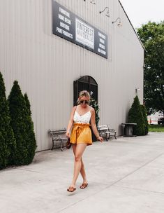 a woman walking in front of a building wearing sunglasses and a yellow skirt with her hand on her hip