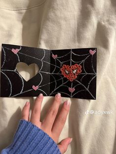 a hand is holding an open card with hearts and spider webs on the inside