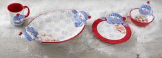 three red and white dishes with blue birds on them sitting in the snow next to two mugs