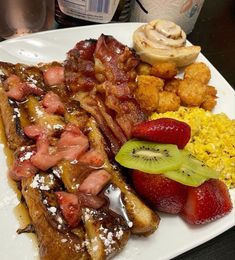 a white plate topped with french toast, strawberries and other breakfast foods next to a cup of coffee